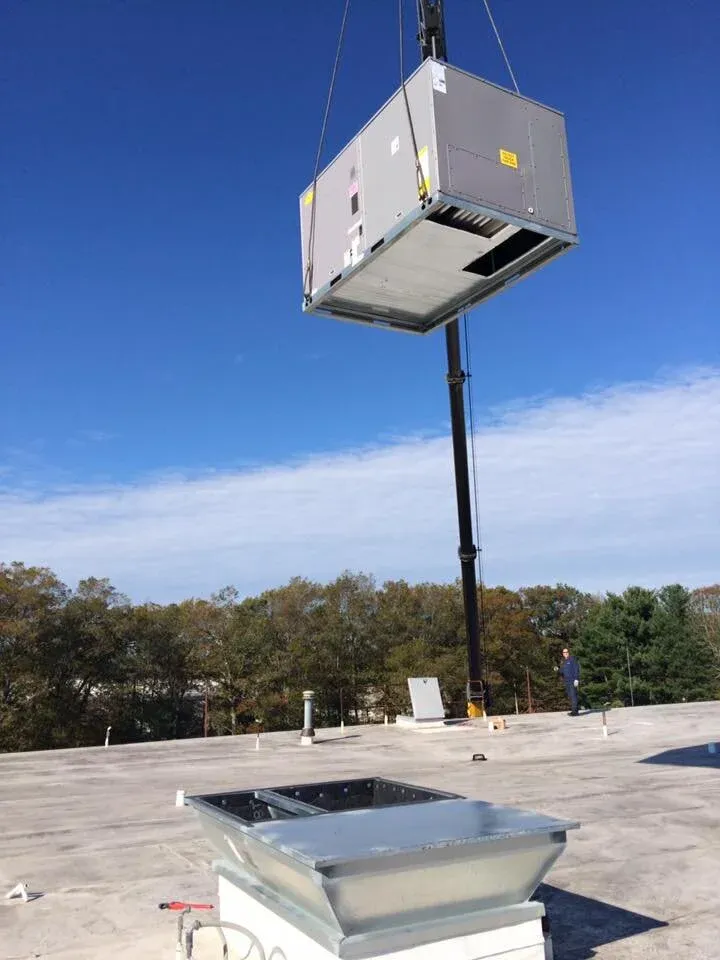 Rooftop HVAC unit being lifted by a crane onto a building roof.