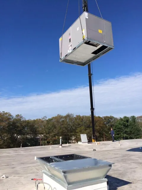 Rooftop HVAC unit being lifted by a crane onto a building roof.