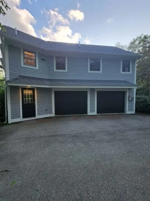 Two-story gray house with a large driveway and three garage doors at dusk