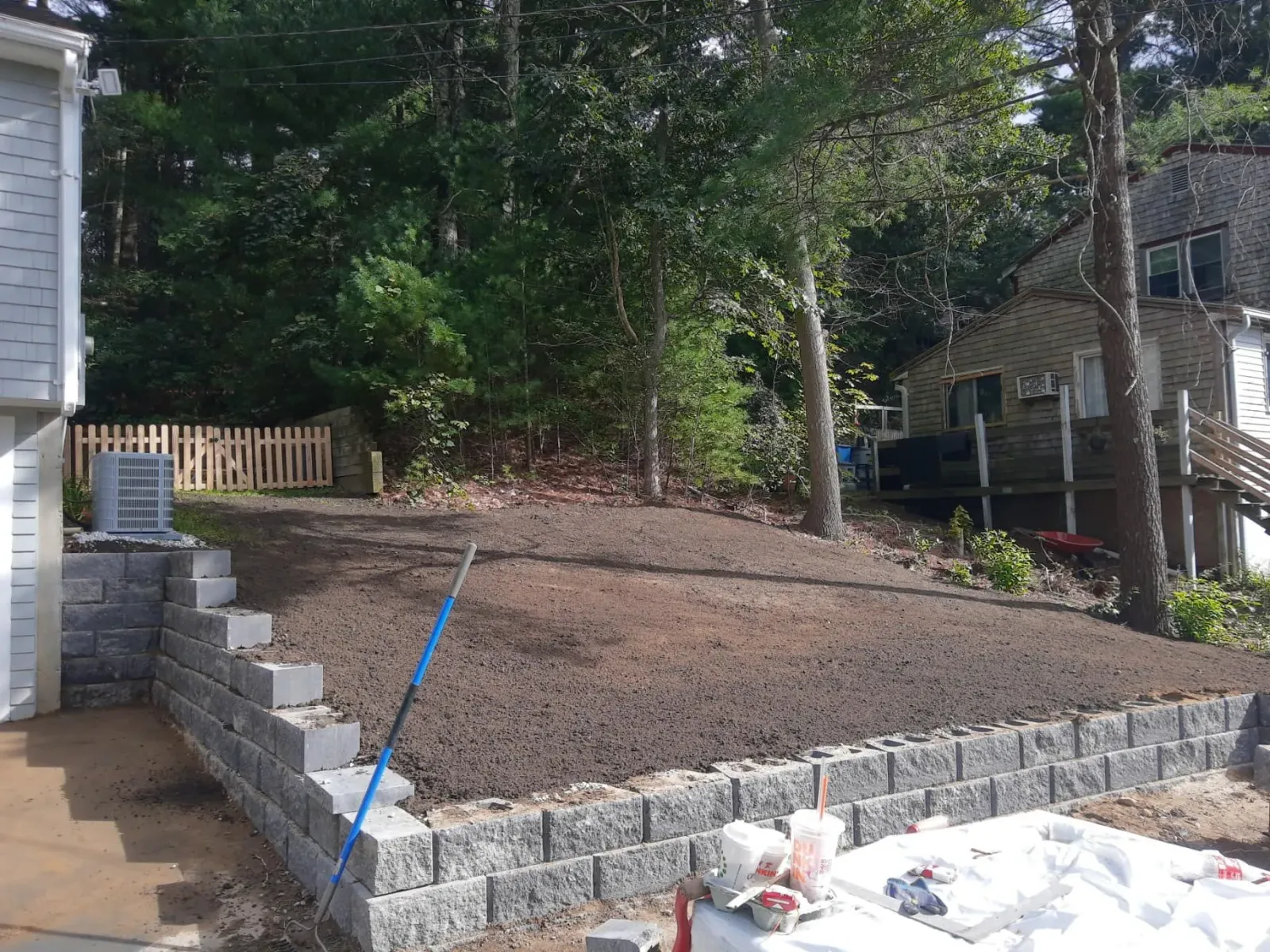 Retaining wall and newly seeded lawn on a sloped yard, near a house and trees.