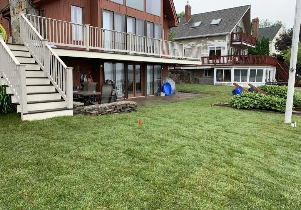 Two-story house with large windows and a wraparound deck, overlooking a lawn with some yard equipment.