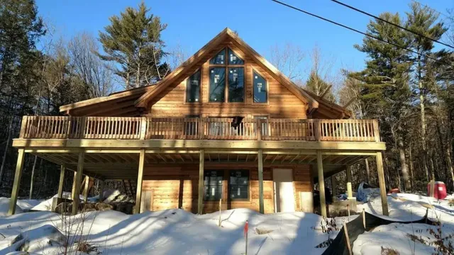 A large log cabin with a large deck is surrounded by snow.