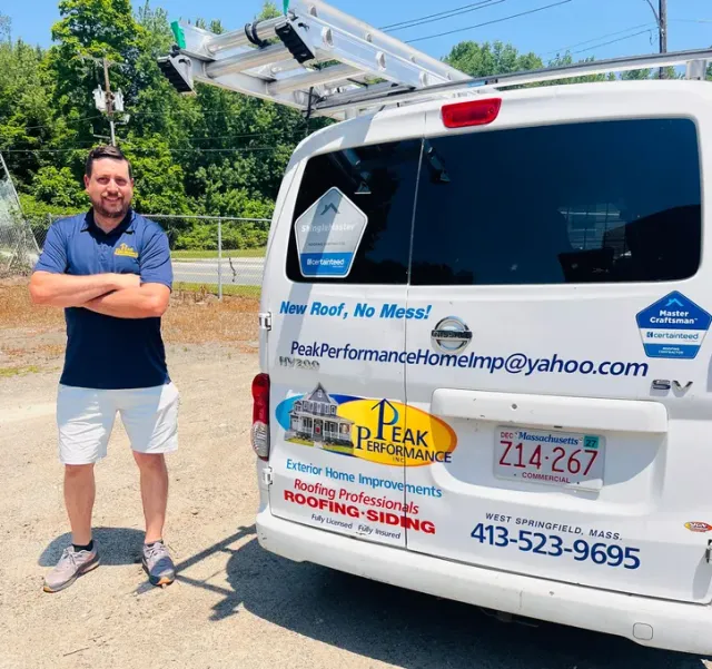 Man standing beside a white utility van with company decals and a ladder on top.