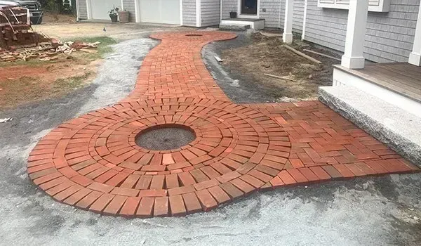 Red brick circular patio with a center drain, curving through a house-side walkway
