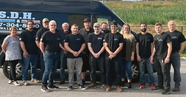Group of people standing in front of a van; some wearing black t-shirts; outdoor setting.