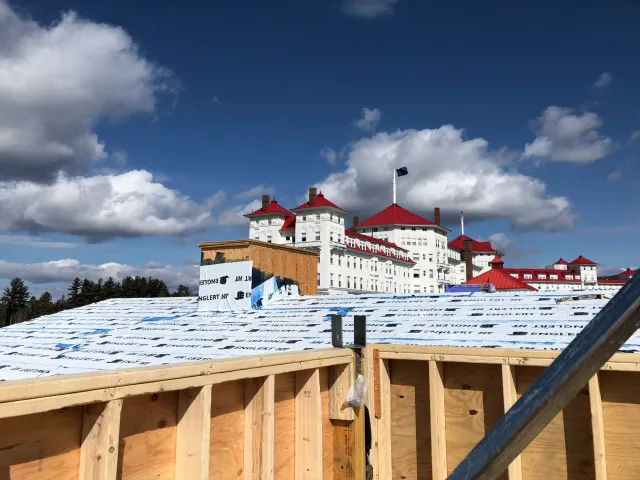 Construction site with view of a large, historic building with red roofs against a blue sky with clouds.