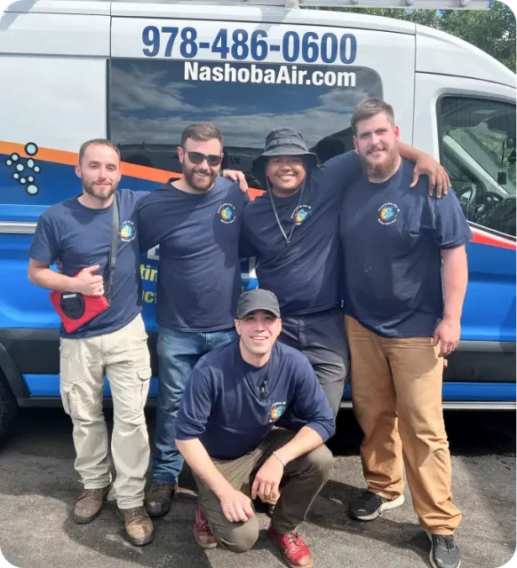 Five people in matching blue shirts pose together in front of a Nashoba Air van parked outdoors.