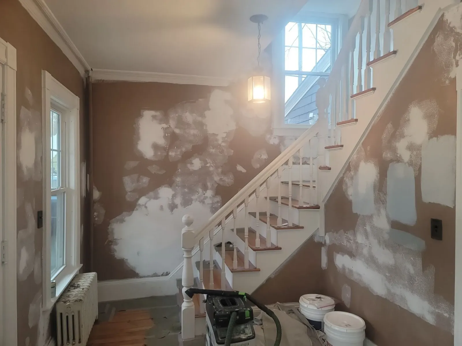 Partially renovated stairwell with patched walls, white stairs, and construction materials on the floor