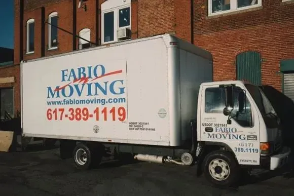 White moving truck parked outside a brick building;