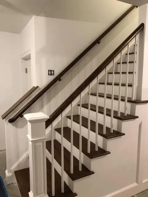 Interior staircase with dark wood steps, white balusters, and a brown handrail against white walls