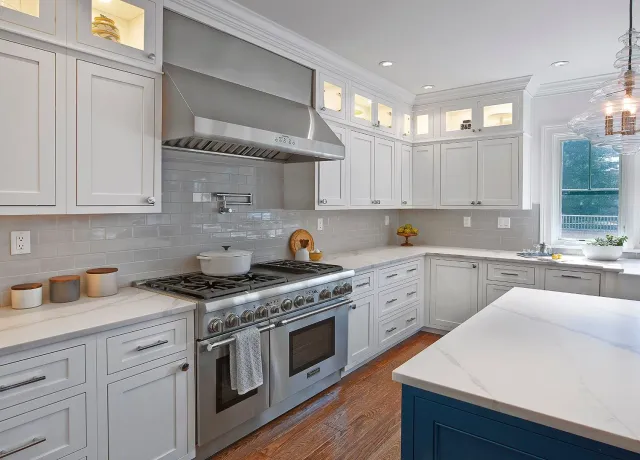Bright white modern kitchen with stainless steel stove, large island, and hanging light fixture