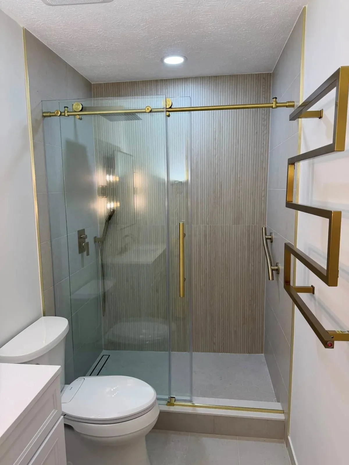 Frameless glass shower with textured tile walls, gold sliding door hardware, and heated towel rack