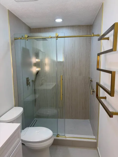 Frameless glass shower with textured tile walls, gold sliding door hardware, and heated towel rack