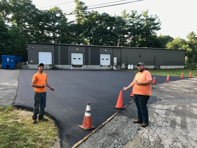 Two men are standing in a parking lot with cones in front of a building.