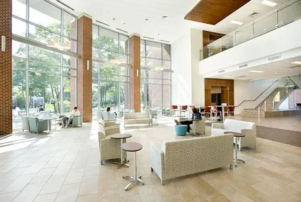 Bright modern lobby with large windows, white lounge seating, and a staircase.
