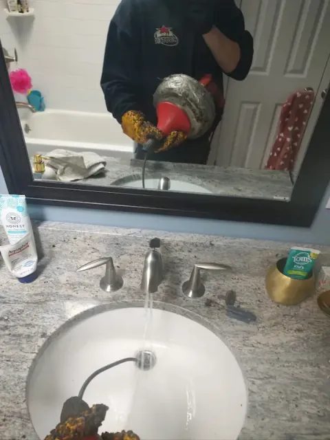 Plumber using drain auger to clear clogged bathroom sink in Norwalk CT