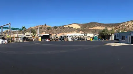Desert roadside lot with parked RVs, low buildings, and hills under a clear sky.