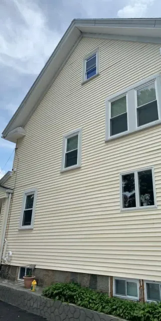 Side view of a beige vinyl-sided house with white-trim windows and a small basement window well.