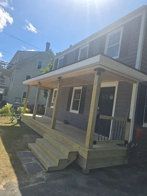 Front exterior of a residential house with a new wooden porch addition and large windows on a sunny day
