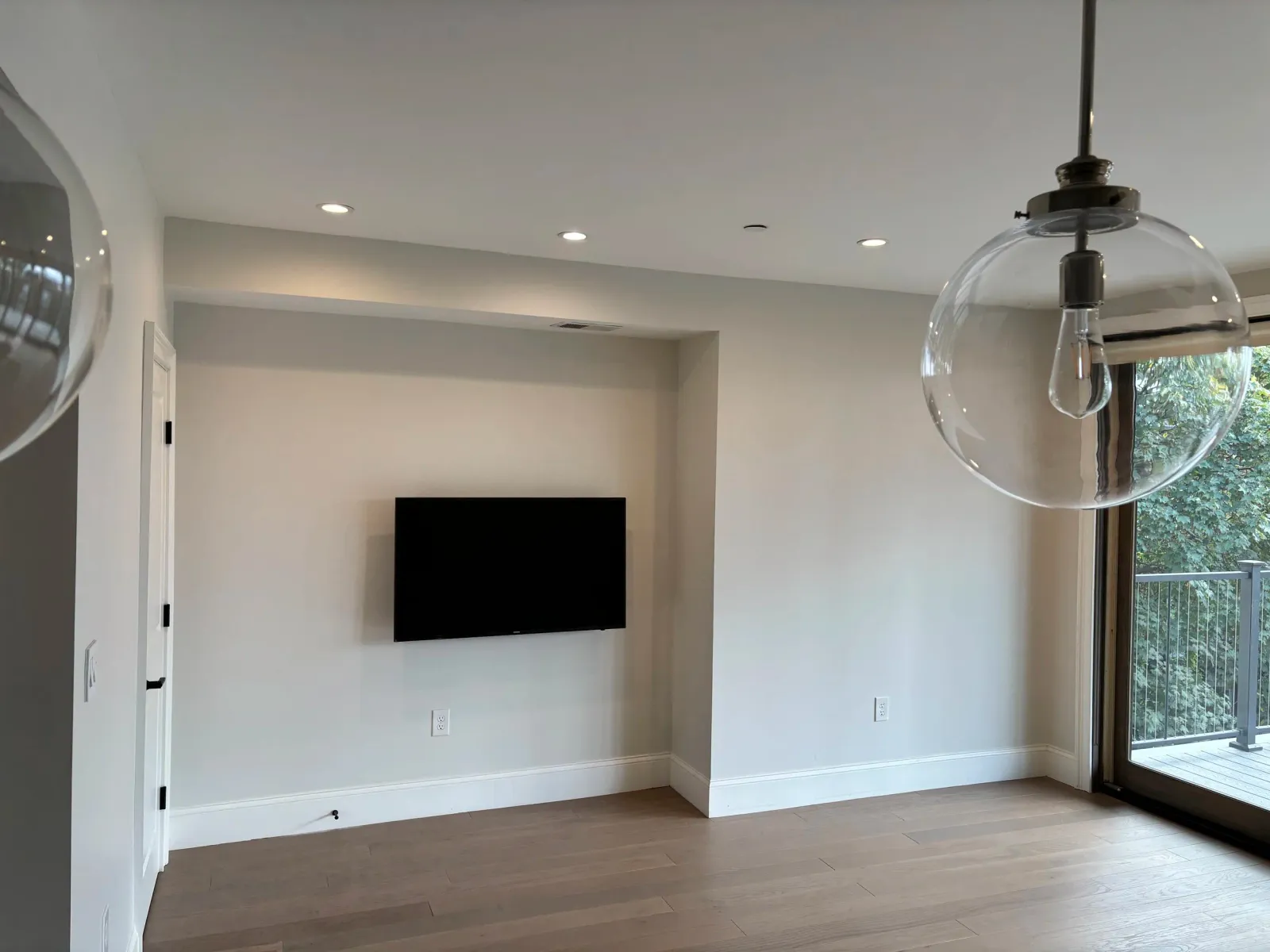 Minimalist interior with wall-mounted TV, large glass pendant lights, and a sliding door leading to a balcony.