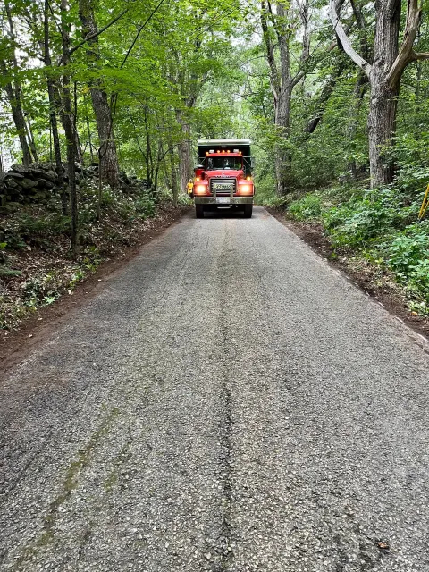 Red truck driving down a gravel road lined by trees.