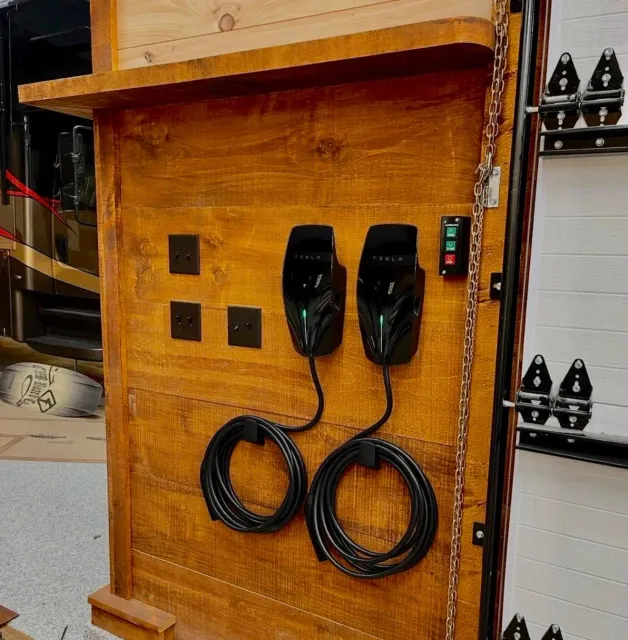 Wall-mounted Tesla electric vehicle chargers with power cords, electrical outlets, and a control panel on a wooden wall.
