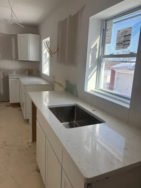 Modern kitchen with white cabinets, marble countertop, and a sink beside a bright window