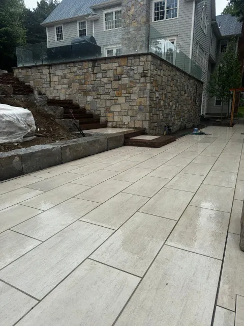 Stone-paved driveway beside a retaining wall and stone house, with a large white bag on the left.