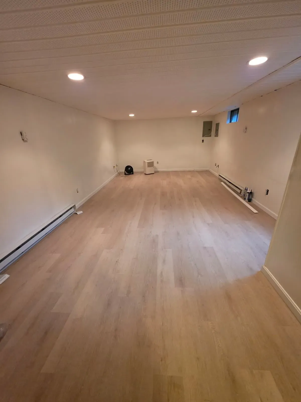 Empty white room with light wood floor, recessed ceiling lights, and small wall fixtures.