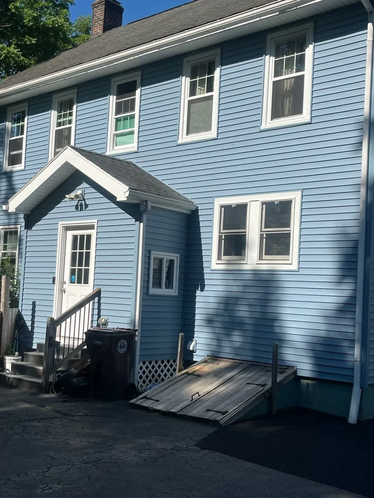 Blue two-story house with a small entrance porch, white trim, and a basement door.
