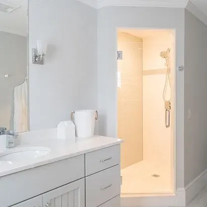 Bright bathroom with vanity, sink, mirror, and an open lit shower stall.