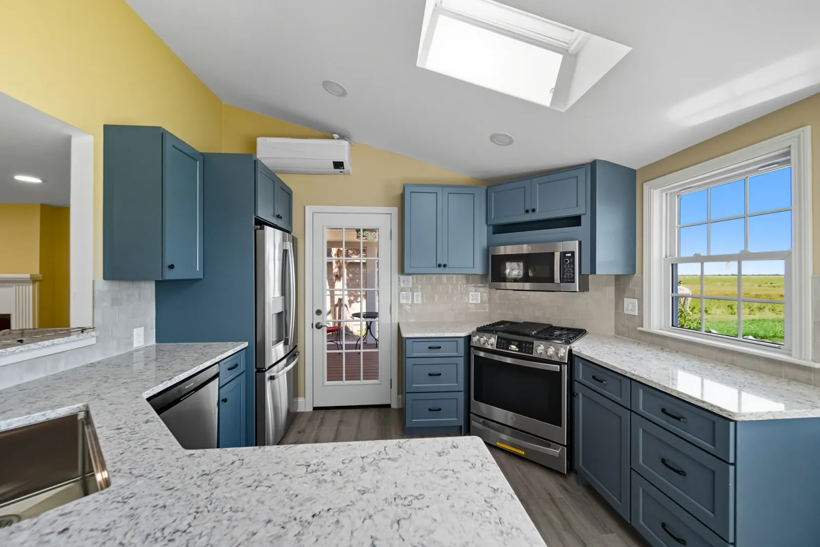 Kitchen with blue cabinets, granite countertops, stainless steel appliances, and a skylight, showcasing a modern renovation by Bradford Construction in West Newbury, MA.