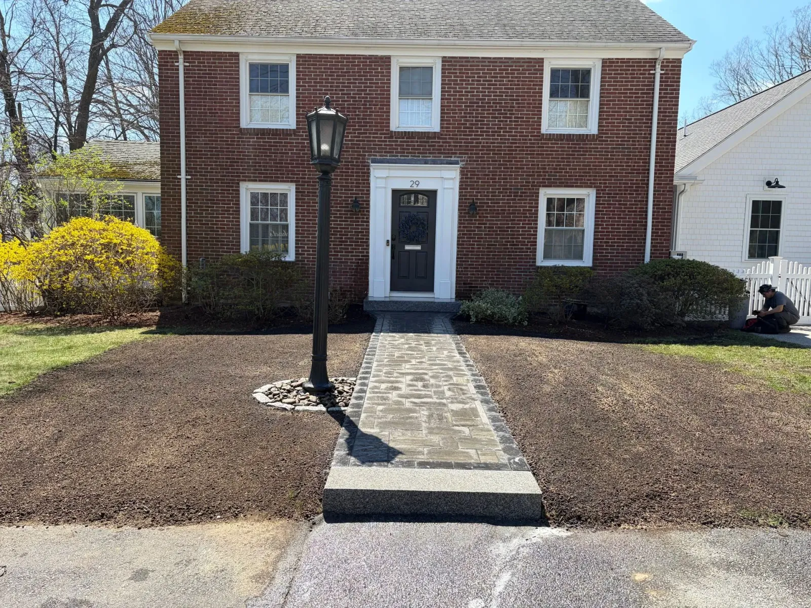 Brick house with central walkway, black lamp post, and bare winter landscaping