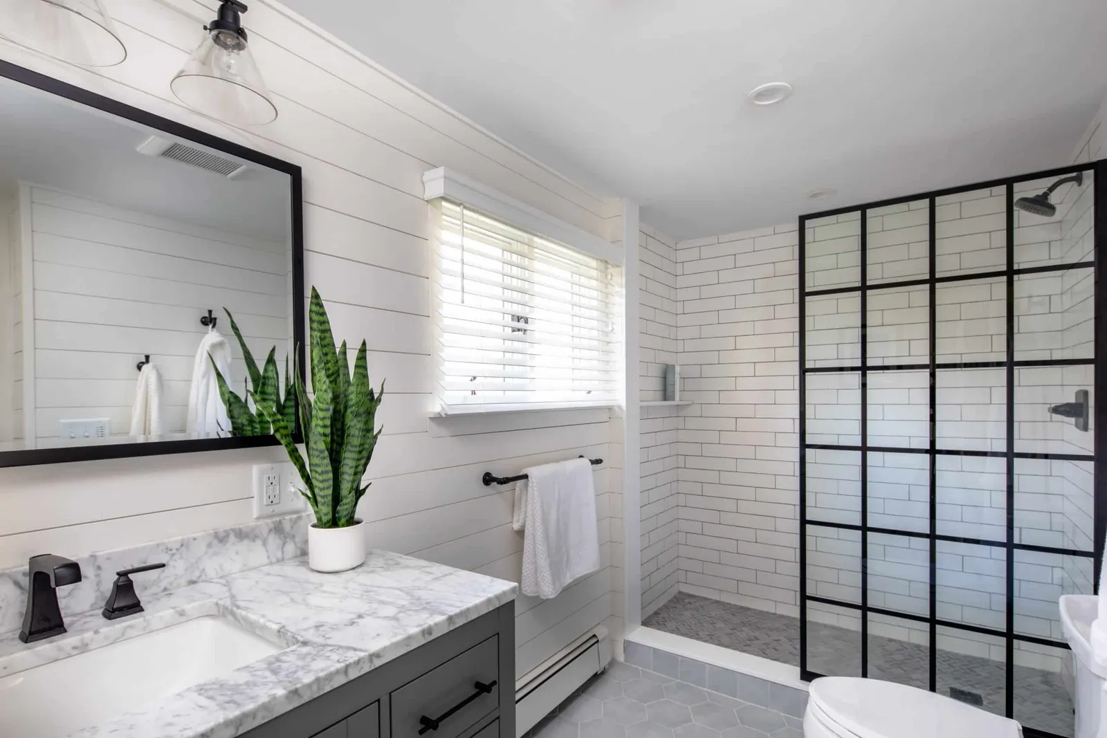 Modern bathroom renovation featuring a marble countertop, black faucet, indoor plant, and glass shower enclosure with white subway tiles, highlighting Harding Builders' craftsmanship.