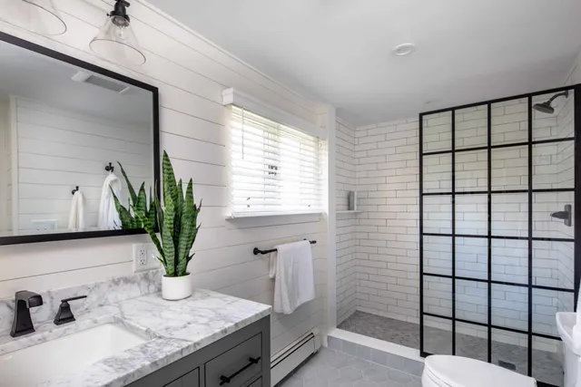 Modern bathroom renovation featuring a marble countertop, black faucet, indoor plant, and glass shower enclosure with white subway tiles, highlighting Harding Builders' craftsmanship.