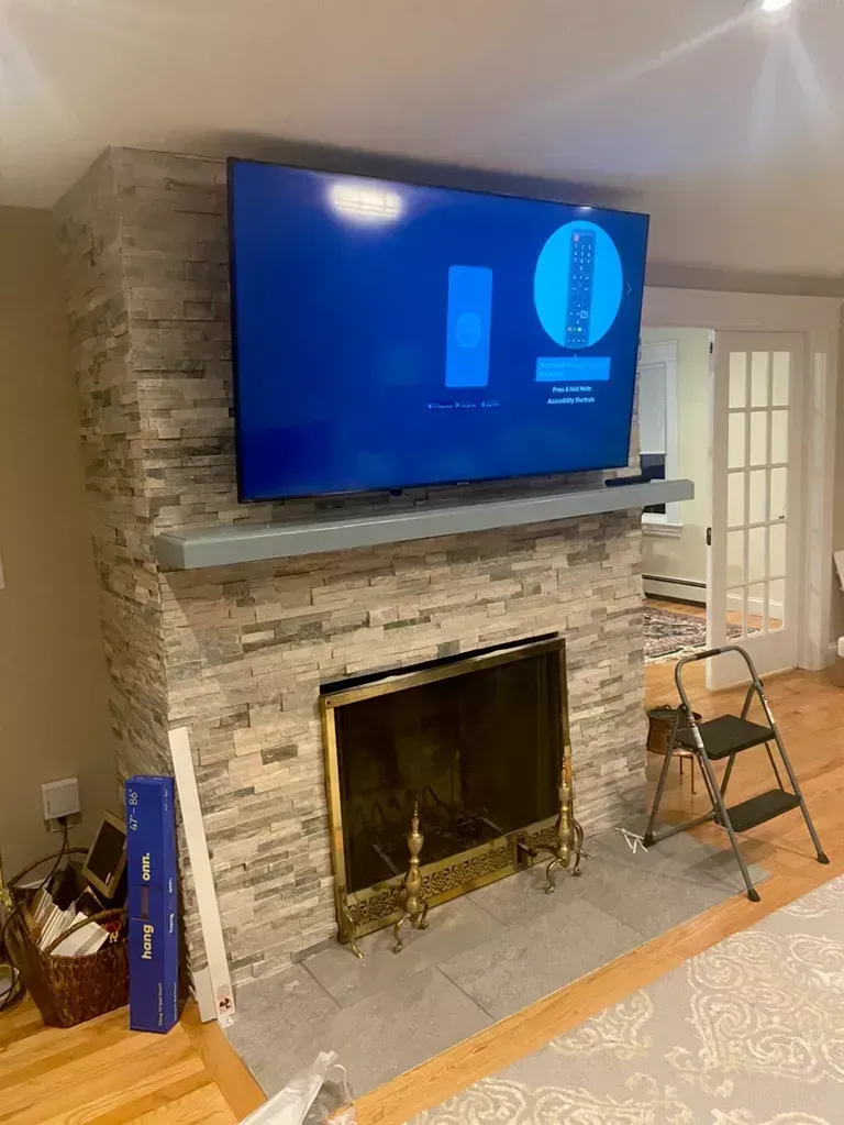 Living room fireplace with mounted TV, stone surround, and a small chair beside it.