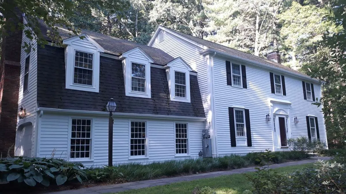 Recently painted two-story house exterior with white siding and dark shutters in a wooded setting
