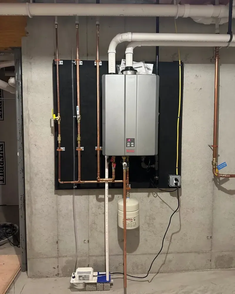 Clean wall-mounted tankless water heater installation with copper piping in a Dunbarton NH home basement by Nault's Plumbing