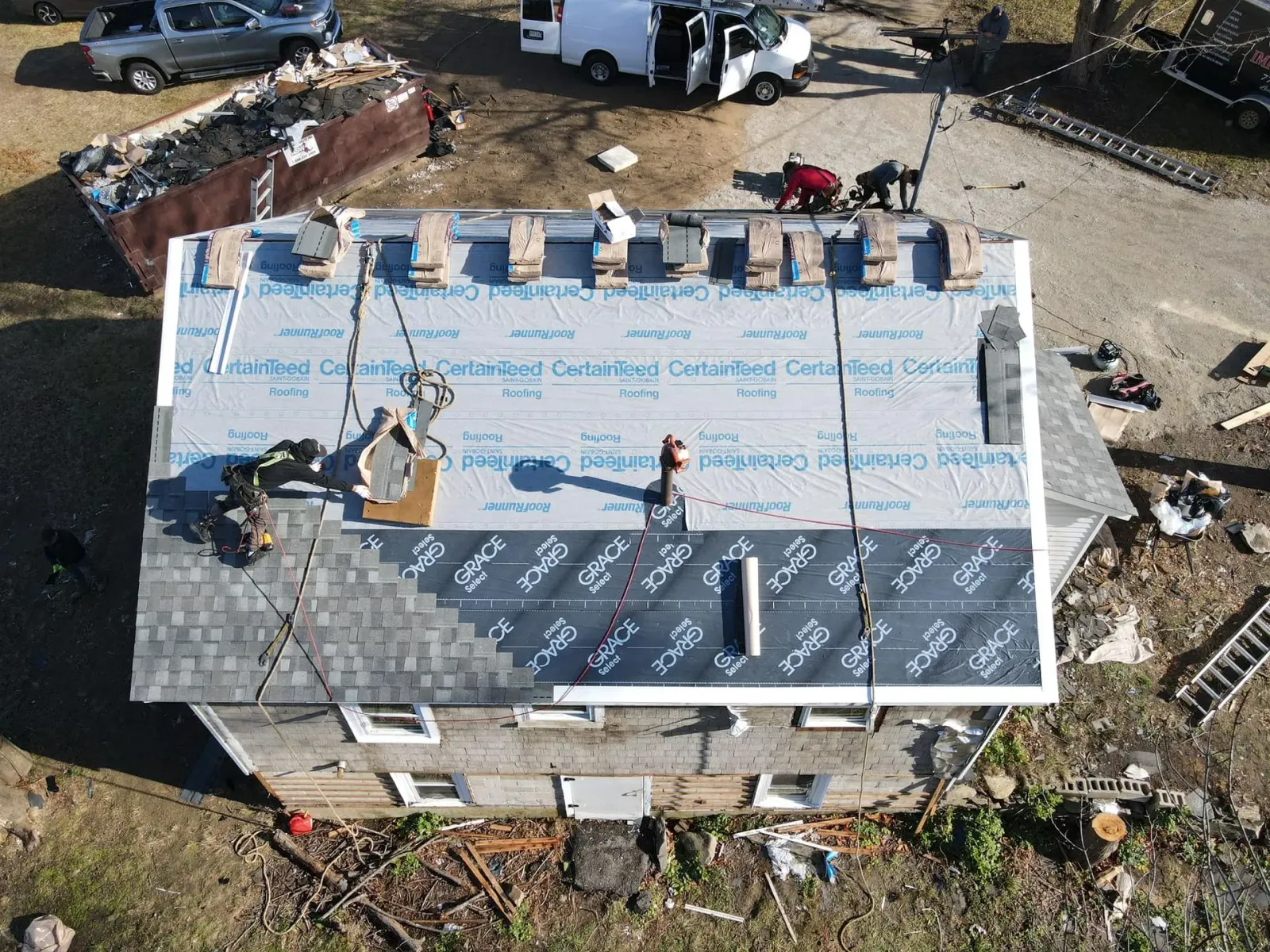 Aerial view of a house roof under construction with workers and materials on top.