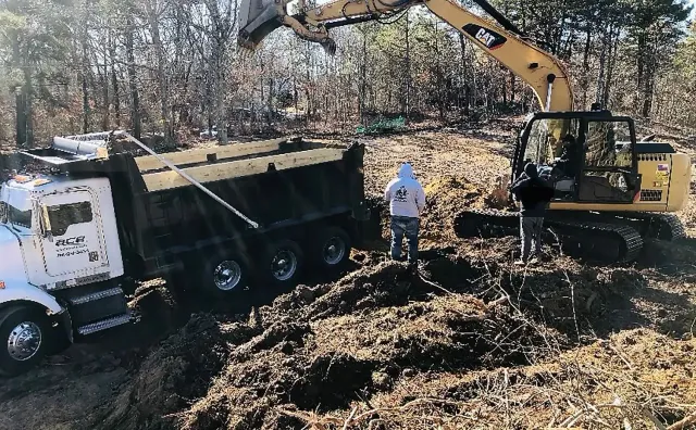 Excavator and dump truck at a muddy construction site with a worker nearby