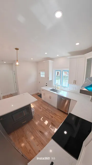 Completed custom kitchen with white cabinetry, quartz countertops, hardwood floors, and a contrasting island