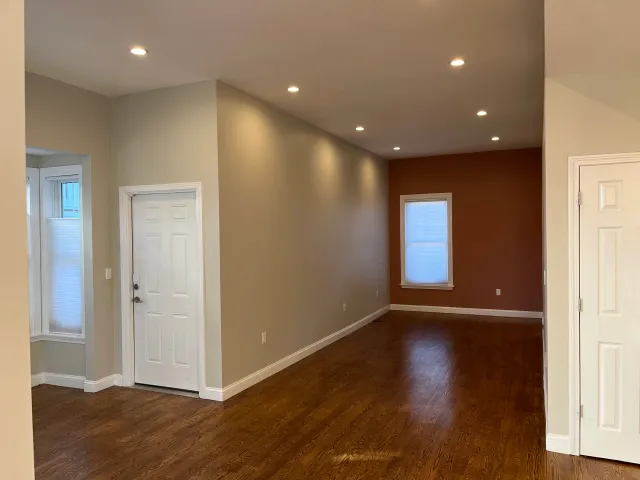 Empty room with hardwood floors, recessed lighting, beige walls, a white door, and a window with blinds.