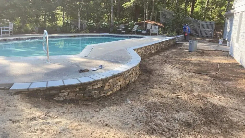 Natural stone retaining wall following the edge of a pool deck