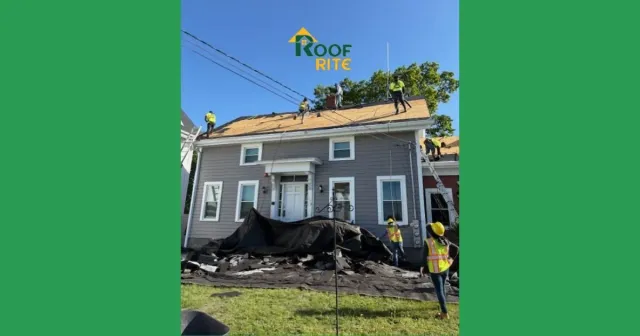 Roofers on a gray house replacing the roof; a safety net is in place; sunny day.