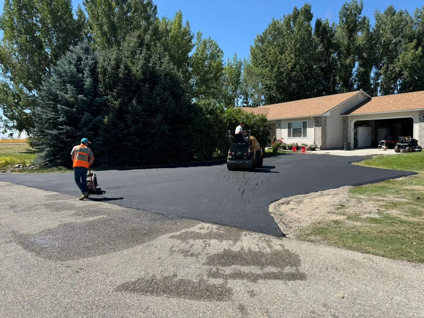 Asphalt paving a driveway in front of a house; workers operate machinery.