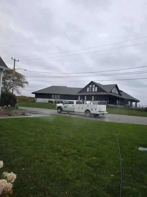 White work truck parked on a green lawn in front of a large house under an overcast sky.