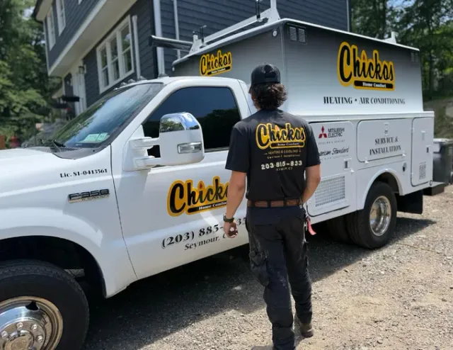 White Chick-fil-A service truck with a worker standing beside it on a sunny residential street.