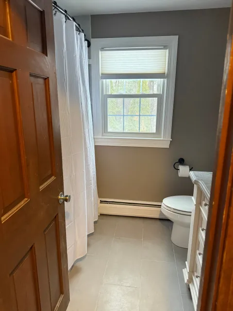 A bathroom with a toilet , sink , shower curtain and window.
