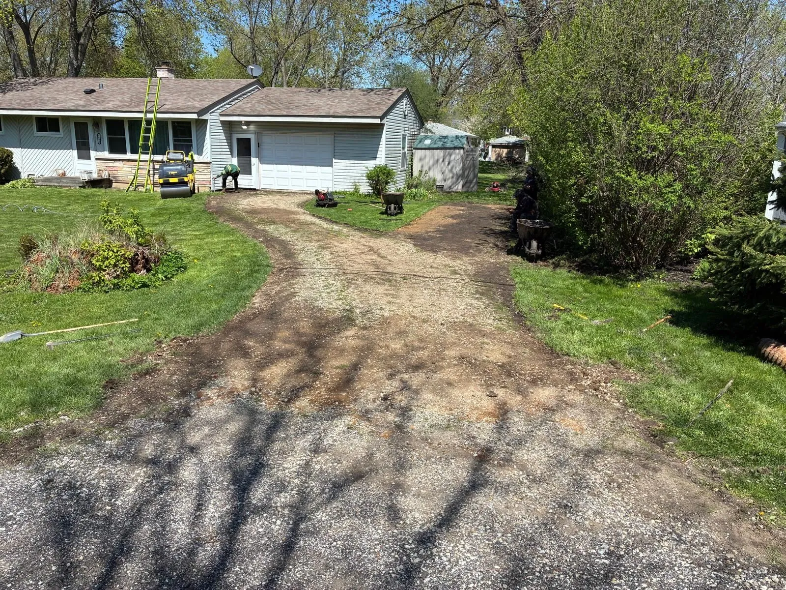 Front yard with a curved gravel driveway leading to a white house and garage, surrounded by green trees and grass