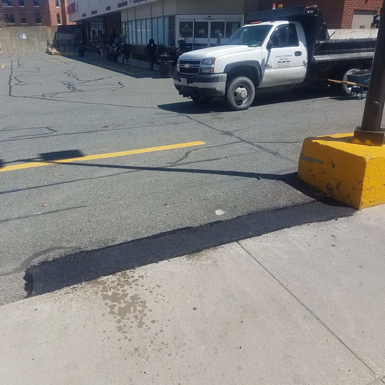 White pickup truck near a building beside a cracked parking lot with yellow painted lines and a curb stop